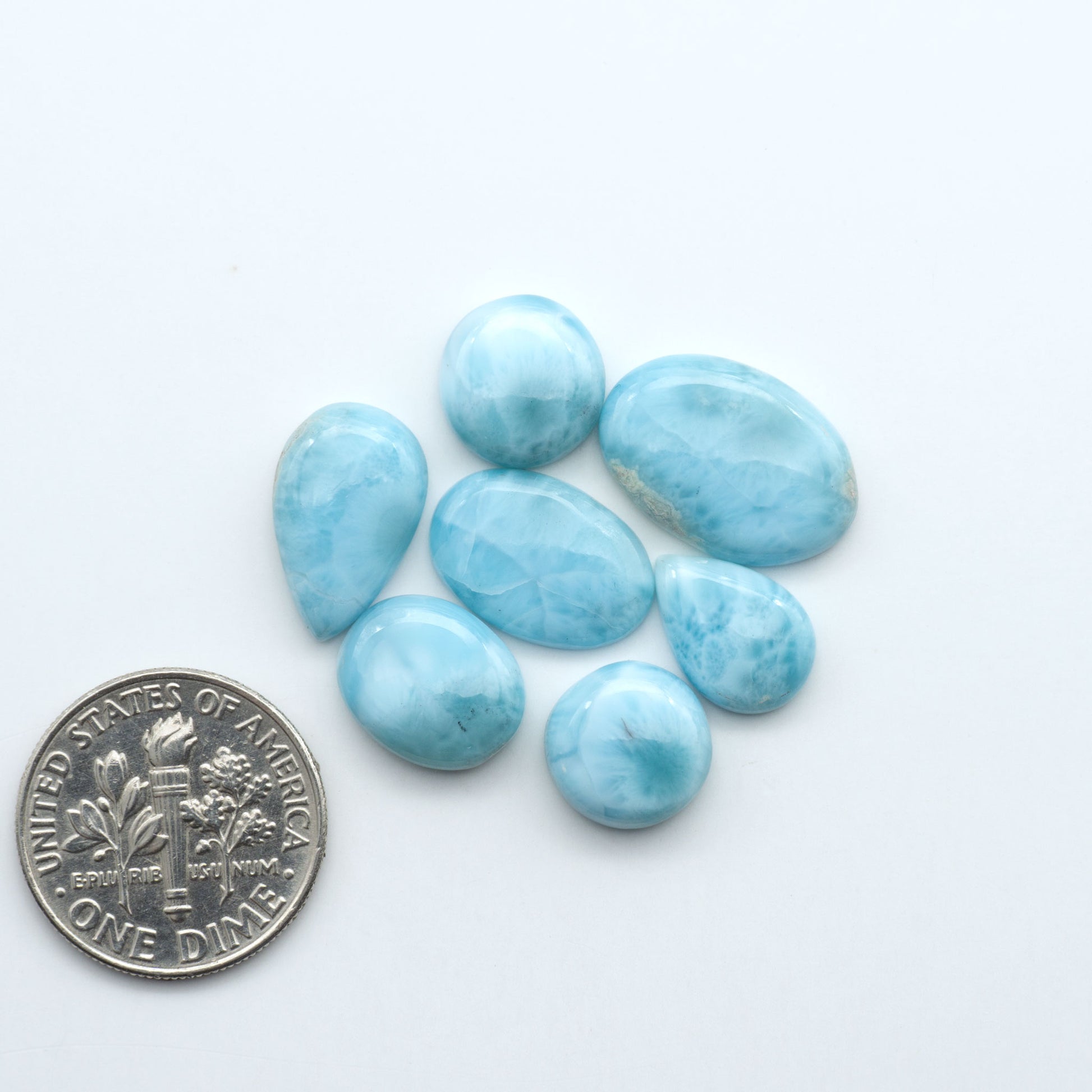 Larimar stone cabochons, cut and polished, blue and white gemstones on a white background, with a US dime for scale