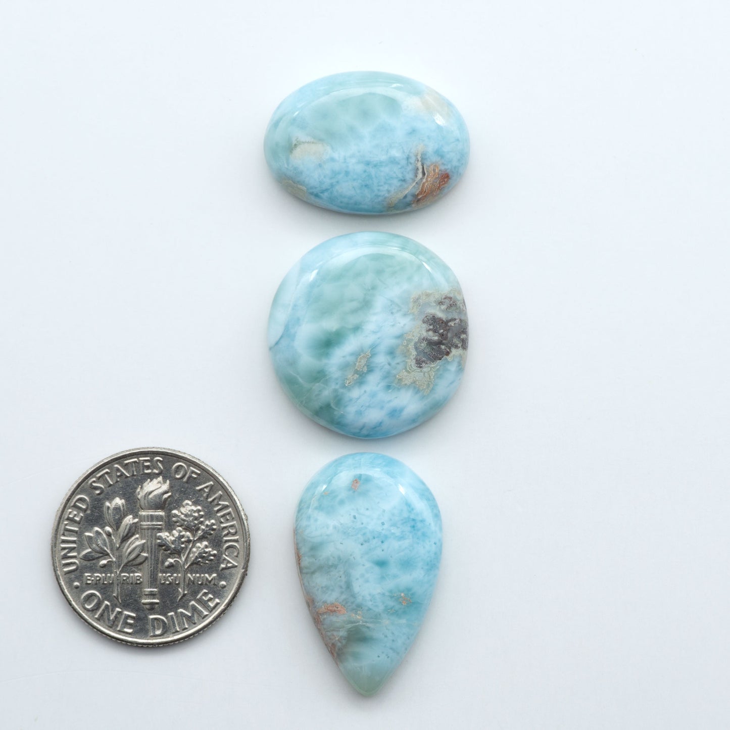 Larimar stone cabochons, cut and polished, blue and white gemstones on a white background, with a US dime for scale