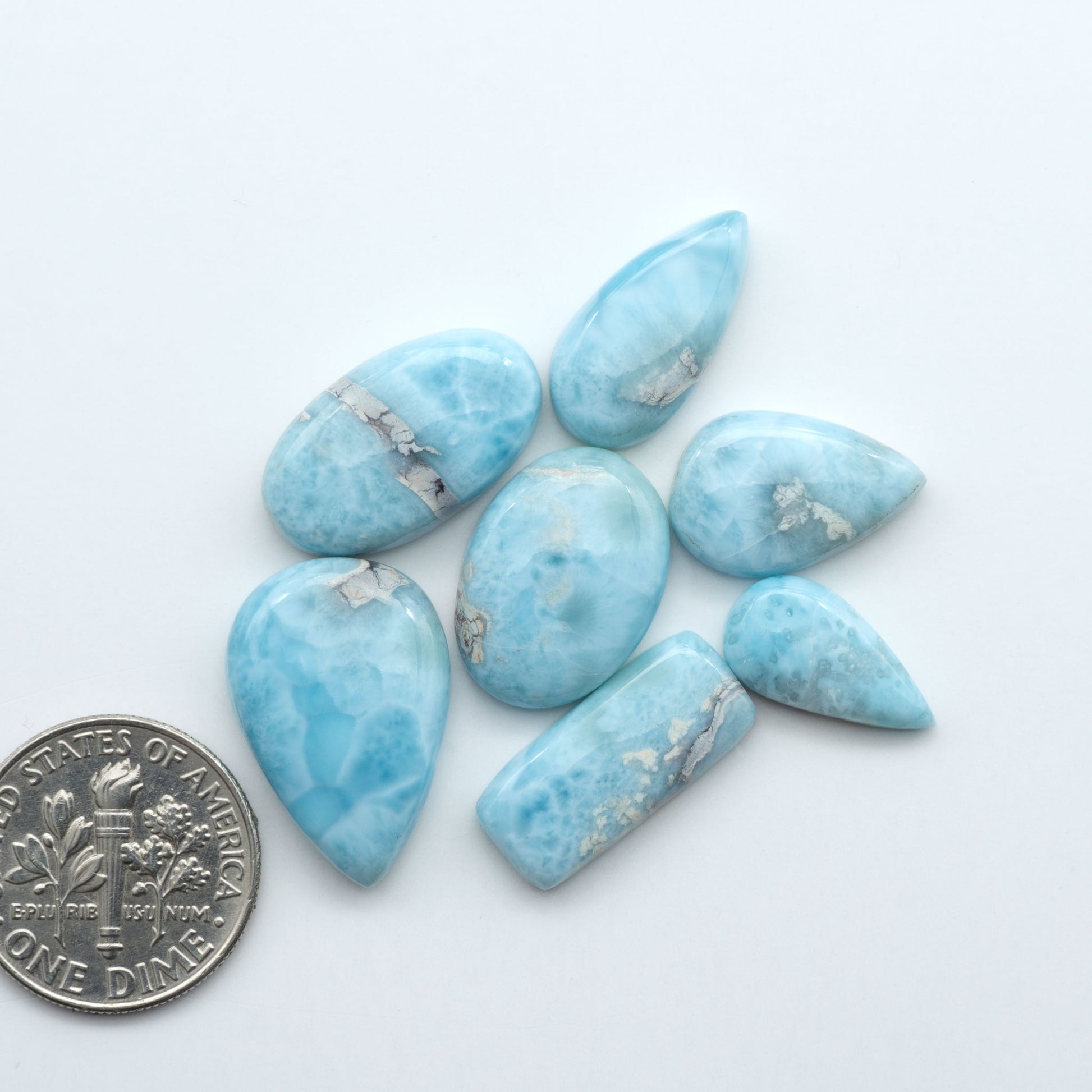 Larimar stone cabochons, cut and polished, blue and white gemstones on a white background, with a US dime for scale