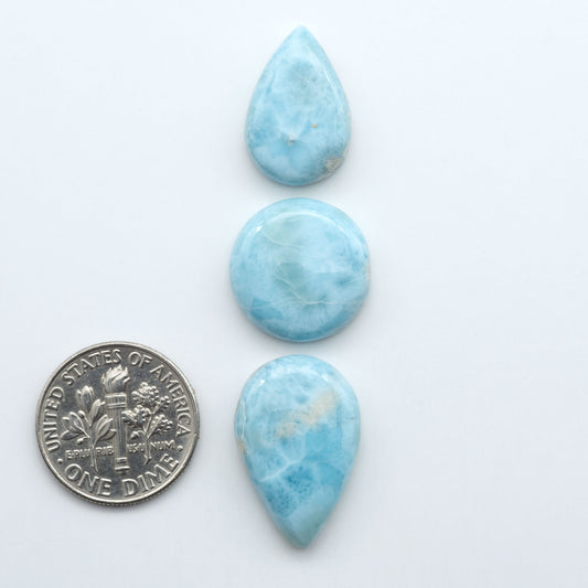 Larimar stone cabochons, cut and polished, blue and white gemstones on a white background, with a US dime for scale