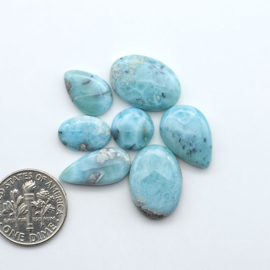 Larimar stone cabochons, cut and polished, blue and white gemstones on a white background, with a US dime for scale