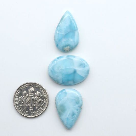 Larimar stone cabochons, cut and polished, blue and white gemstones on a white background, with a US dime for scale