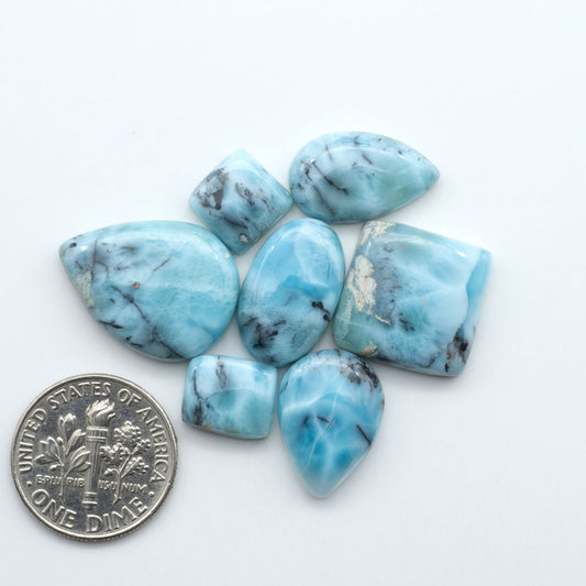 Larimar stone cabochons, cut and polished, blue and white gemstones on a white background, with a US dime for scale