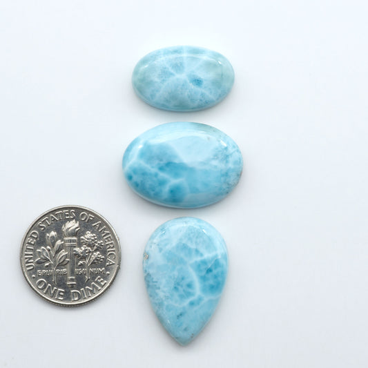 Larimar stone cabochons, cut and polished, blue and white gemstones on a white background, with a US dime for scale
