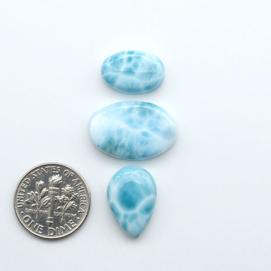 Larimar stone cabochons, cut and polished, blue and white gemstones on a white background, with a US dime for scale