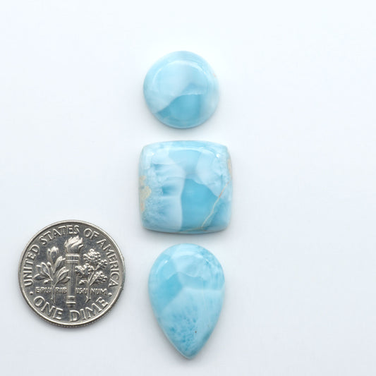 Larimar stone cabochons, cut and polished, blue and white gemstones on a white background, with a US dime for scale