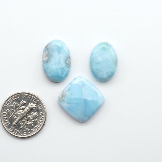 Larimar stone cabochons, cut and polished, blue and white gemstones on a white background, with a US dime for scale