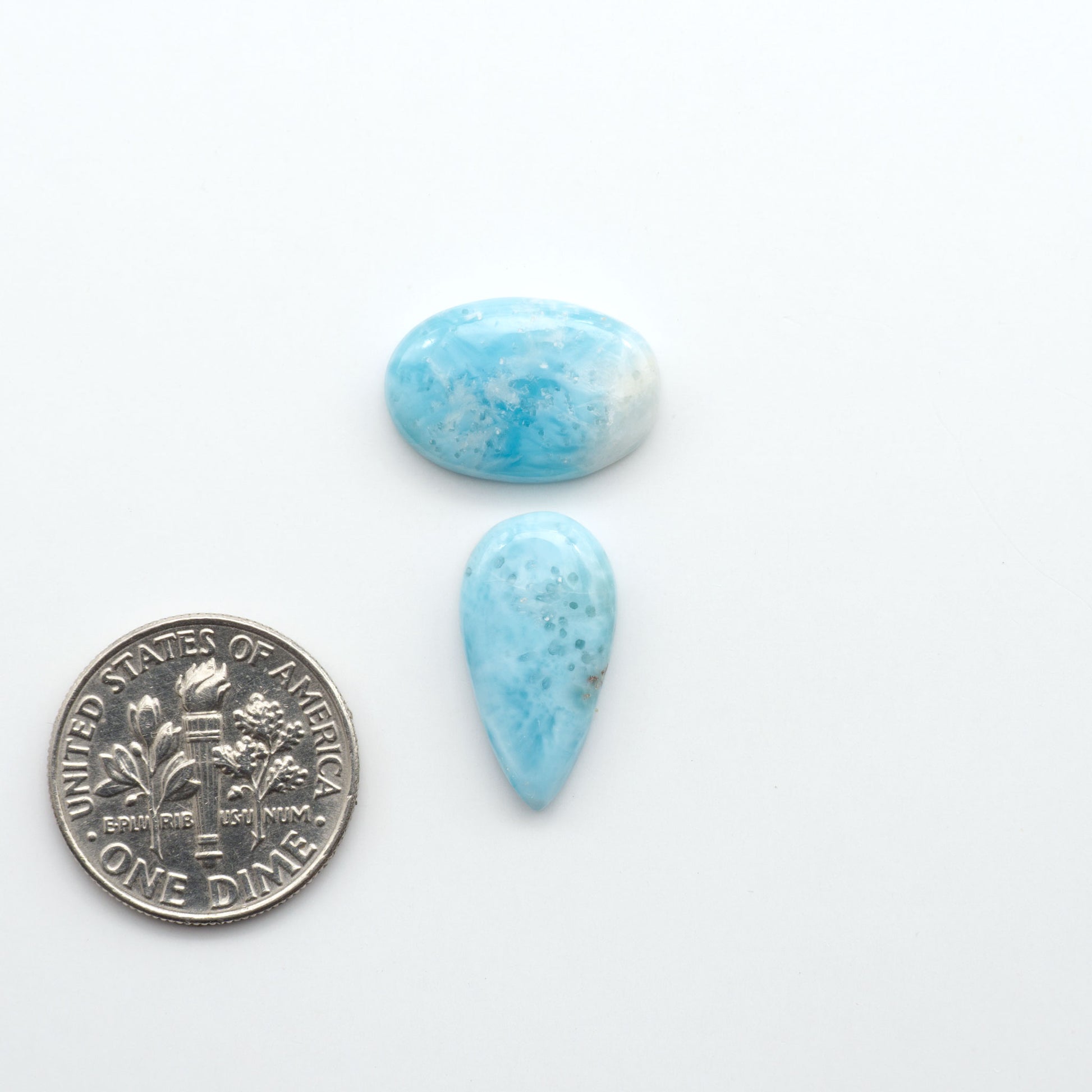 Larimar stone cabochons, cut and polished, blue and white gemstones on a white background, with a US dime for scale