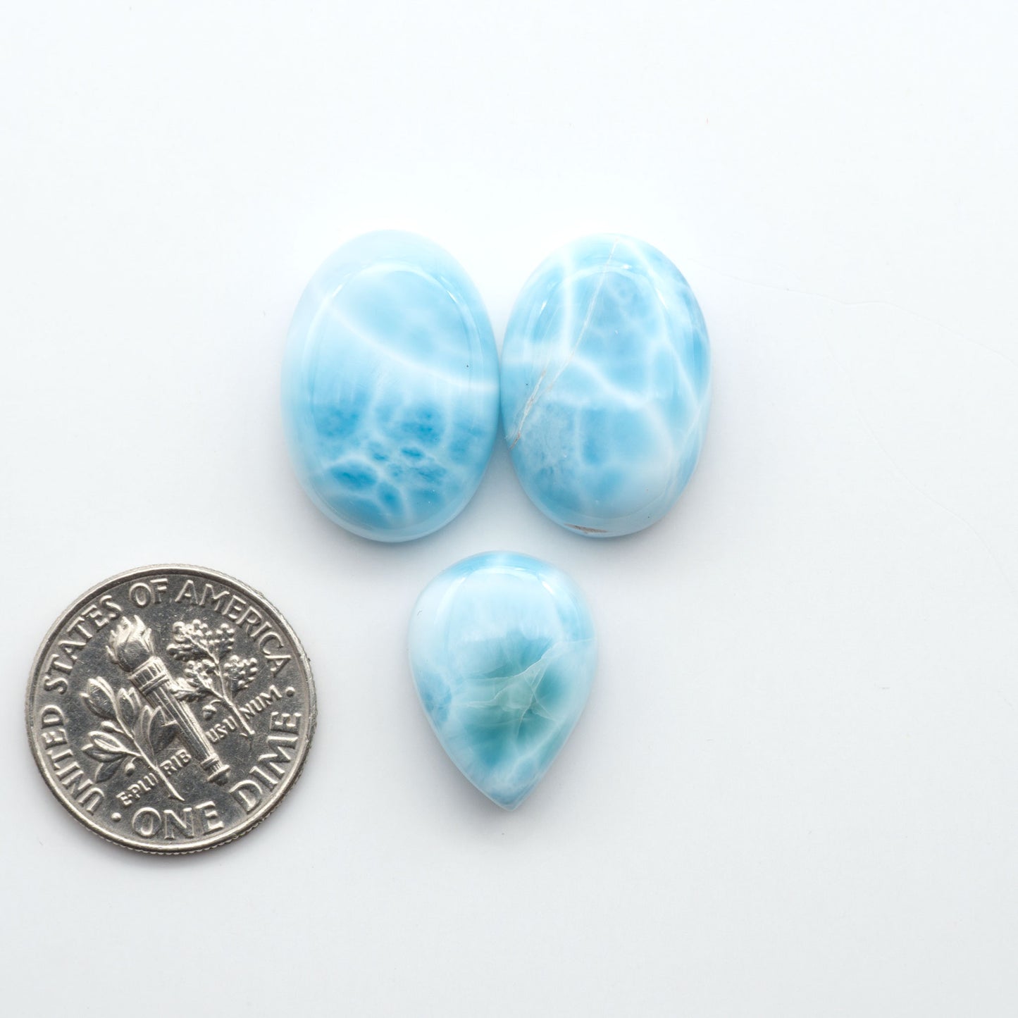 Larimar stone cabochons, cut and polished, blue and white gemstones on a white background, with a US dime for scale