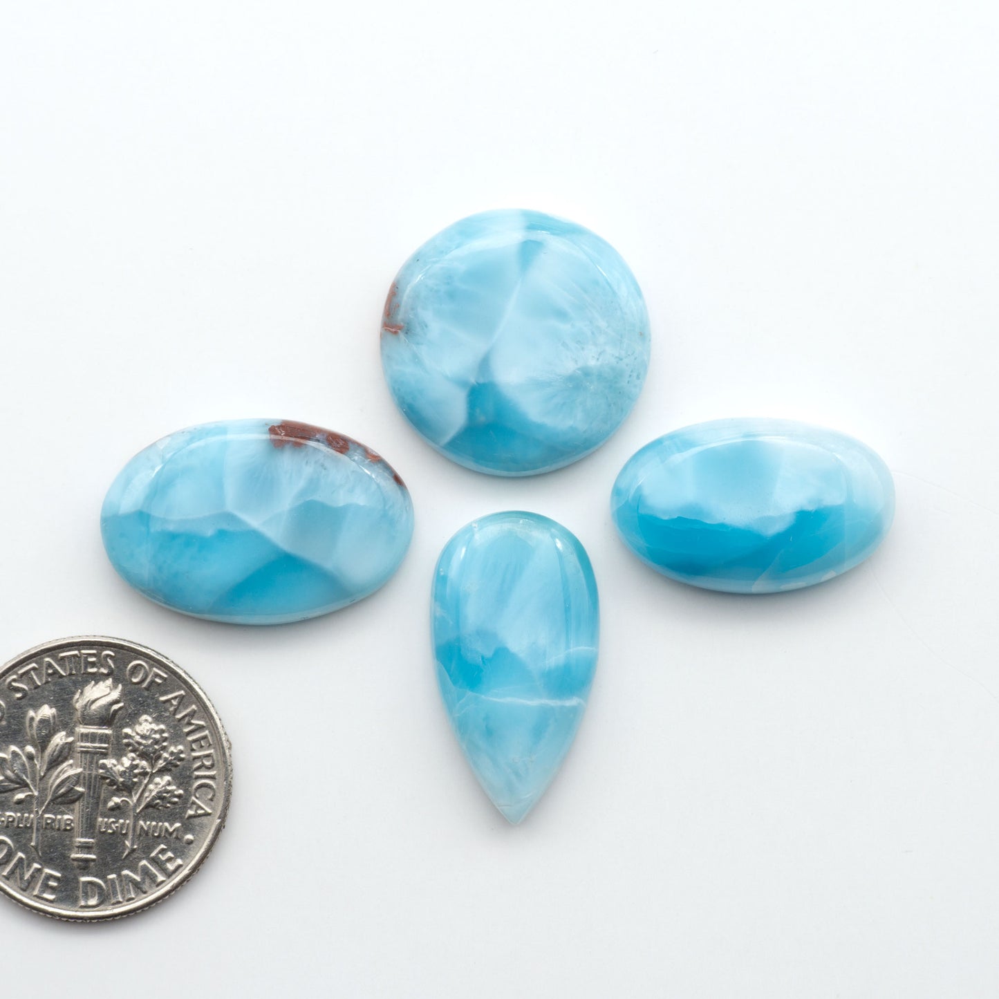Larimar stone cabochons, cut and polished, blue and white gemstones on a white background, with a US dime for scale