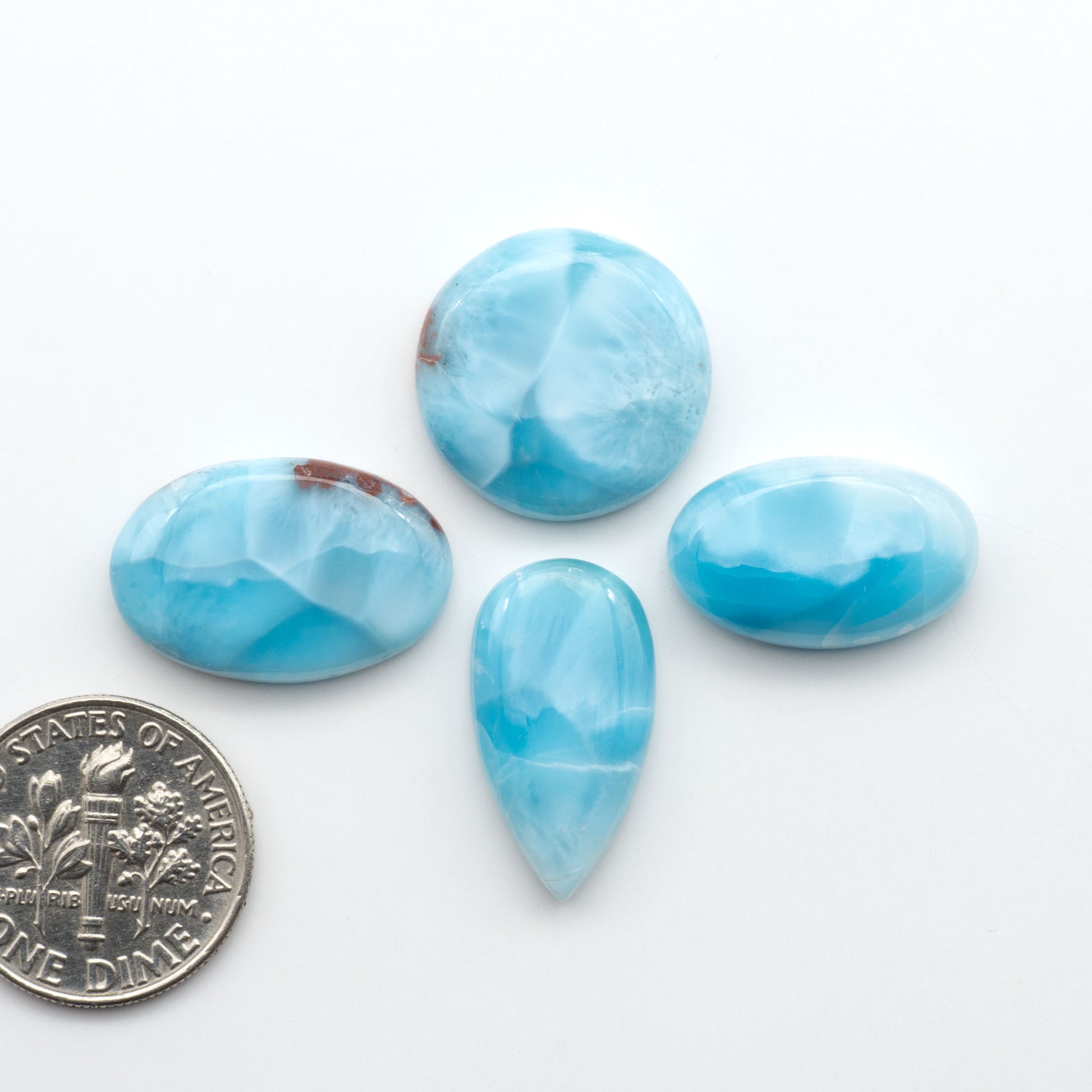Larimar stone cabochons, cut and polished, blue and white gemstones on a white background, with a US dime for scale