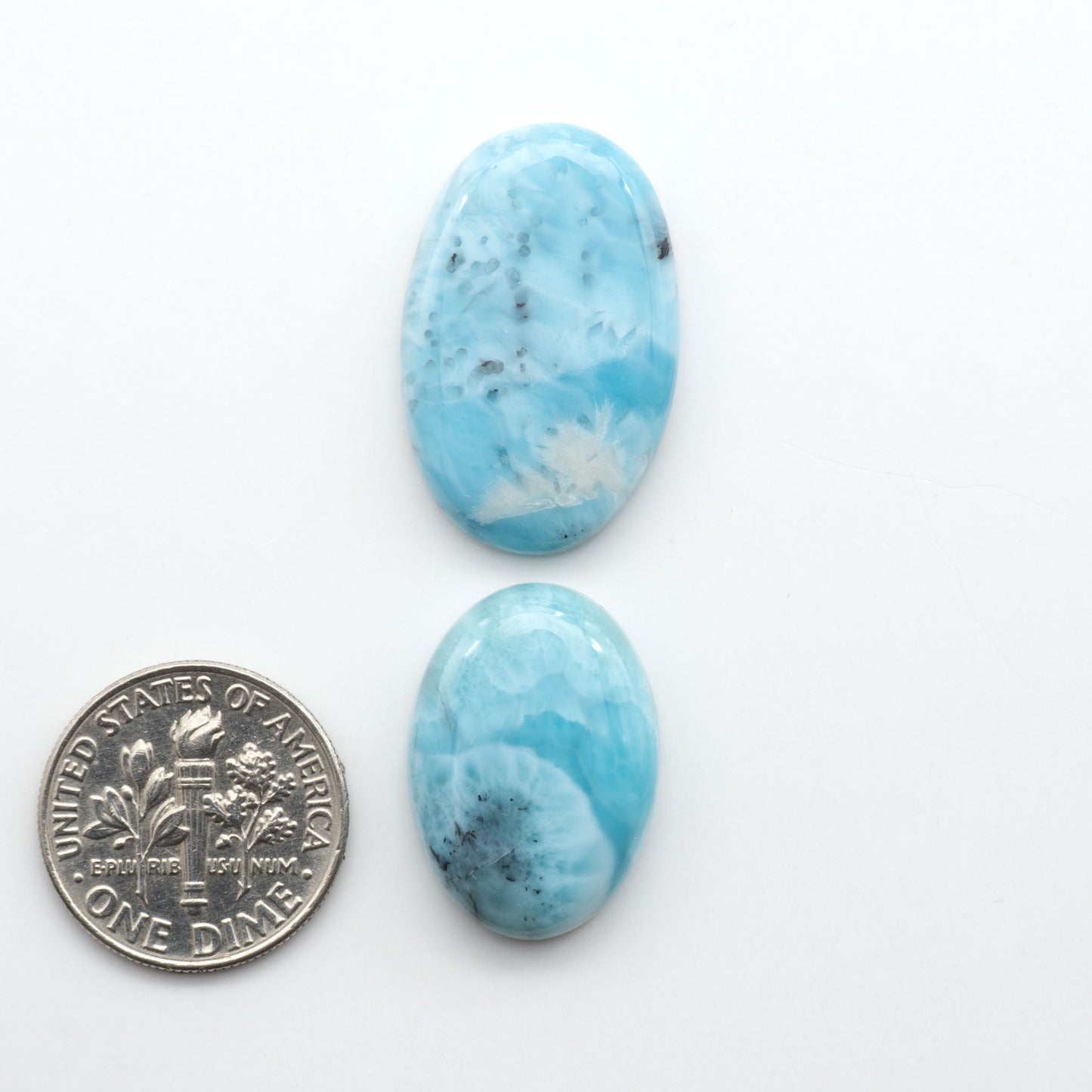Larimar stone cabochons, cut and polished, blue and white gemstones on a white background, with a US dime for scale