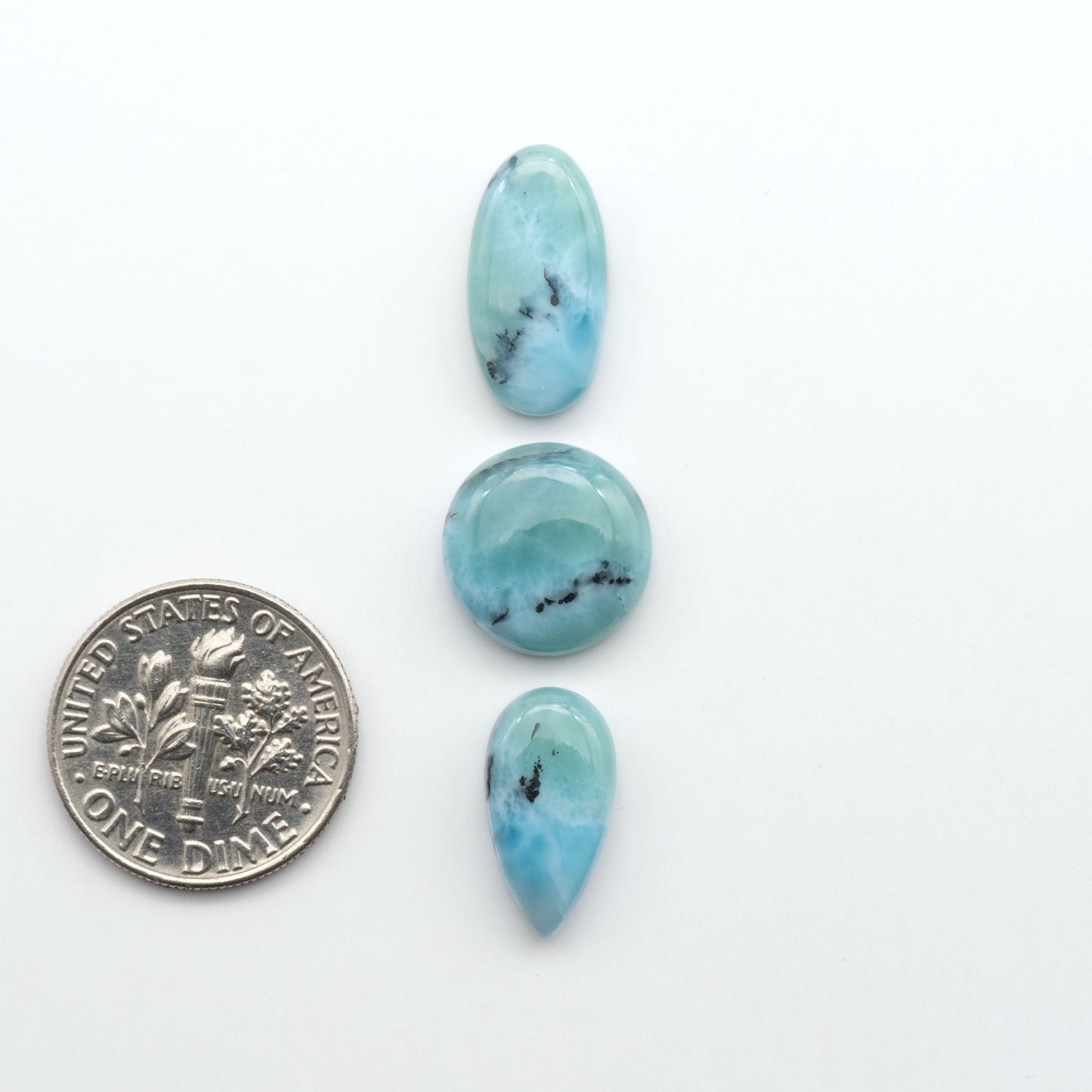 Larimar stone cabochons, cut and polished, blue and white gemstones on a white background, with a US dime for scale