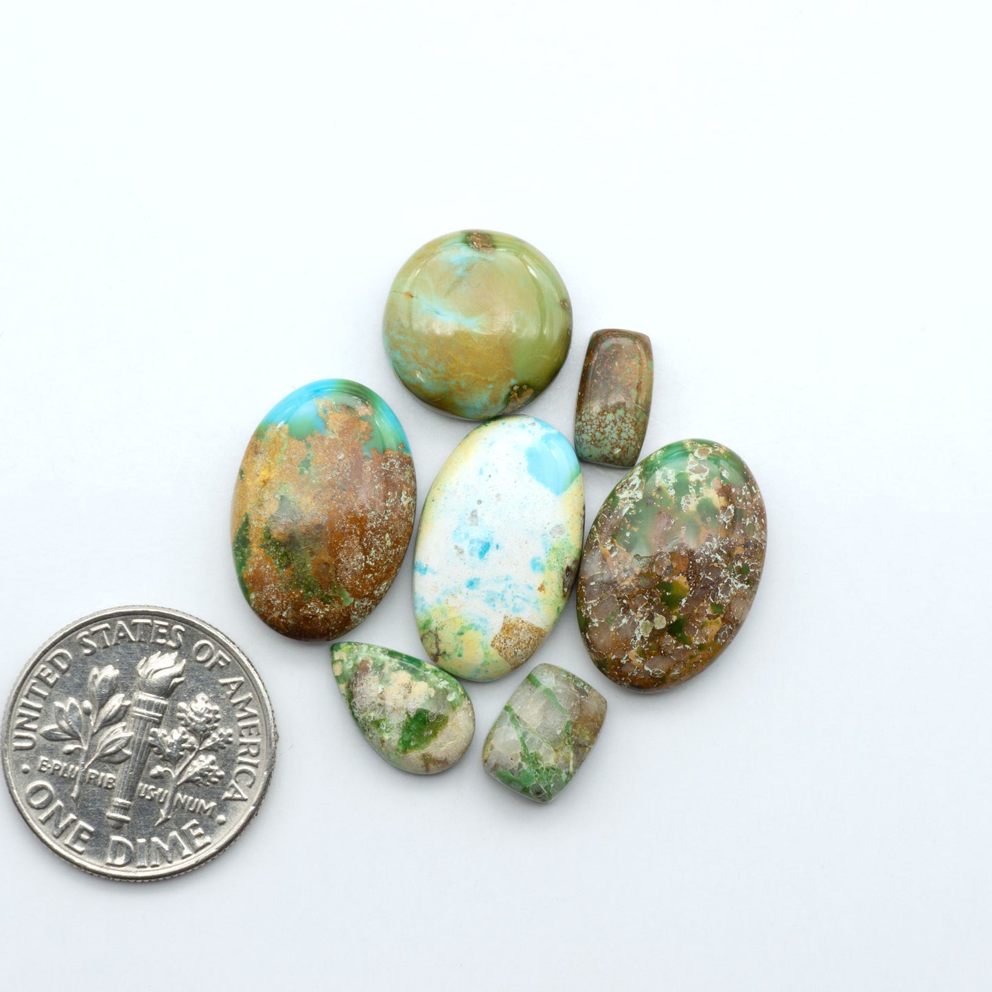 Sonoran Mountain Turquoise cabochons, blue-green color with natural matrix, polished stones on a white background, with a US dime for scale