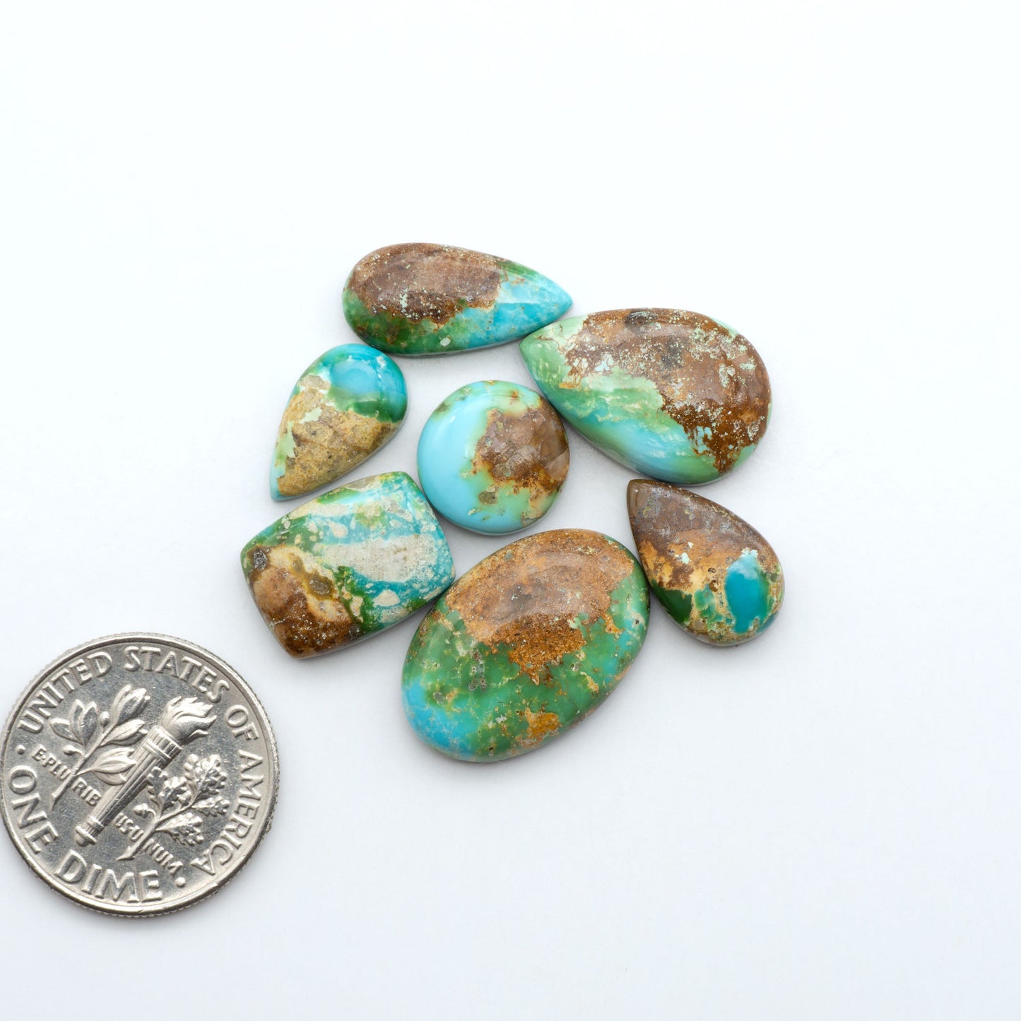 Sonoran Mountain Turquoise cabochons, blue-green color with natural matrix, polished stones on a white background, with a US dime for scale