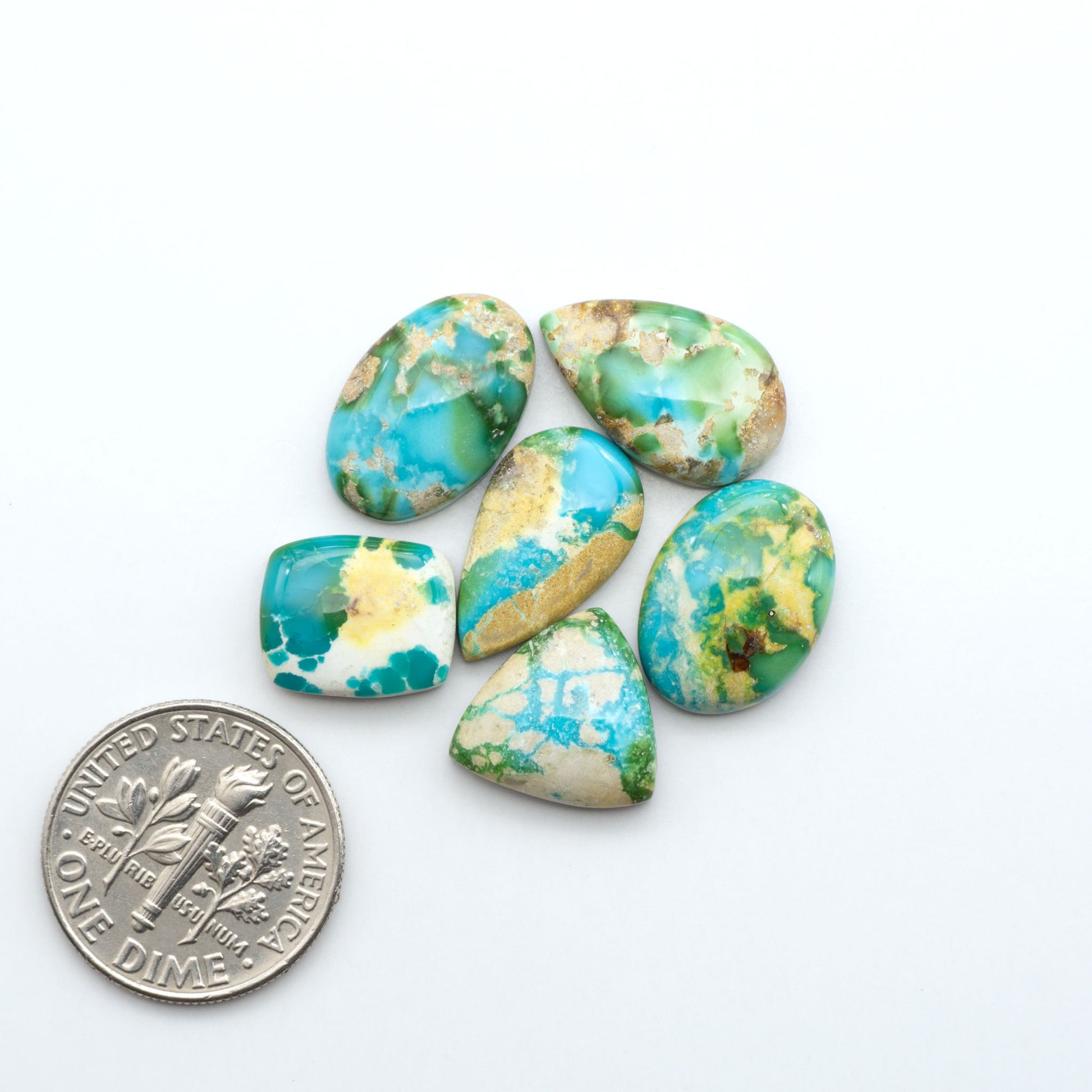 Sonoran Mountain Turquoise cabochons, blue-green color with natural matrix, polished stones on a white background, with a US dime for scale
