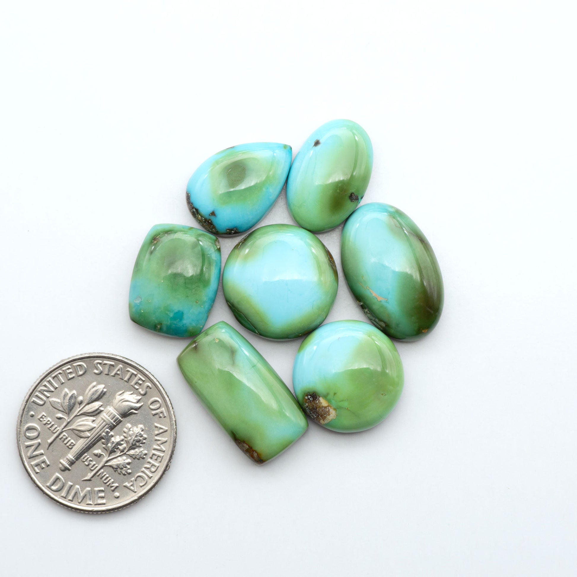 Sonoran Mountain Turquoise cabochons, blue-green color with natural matrix, polished stones on a white background, with a US dime for scale