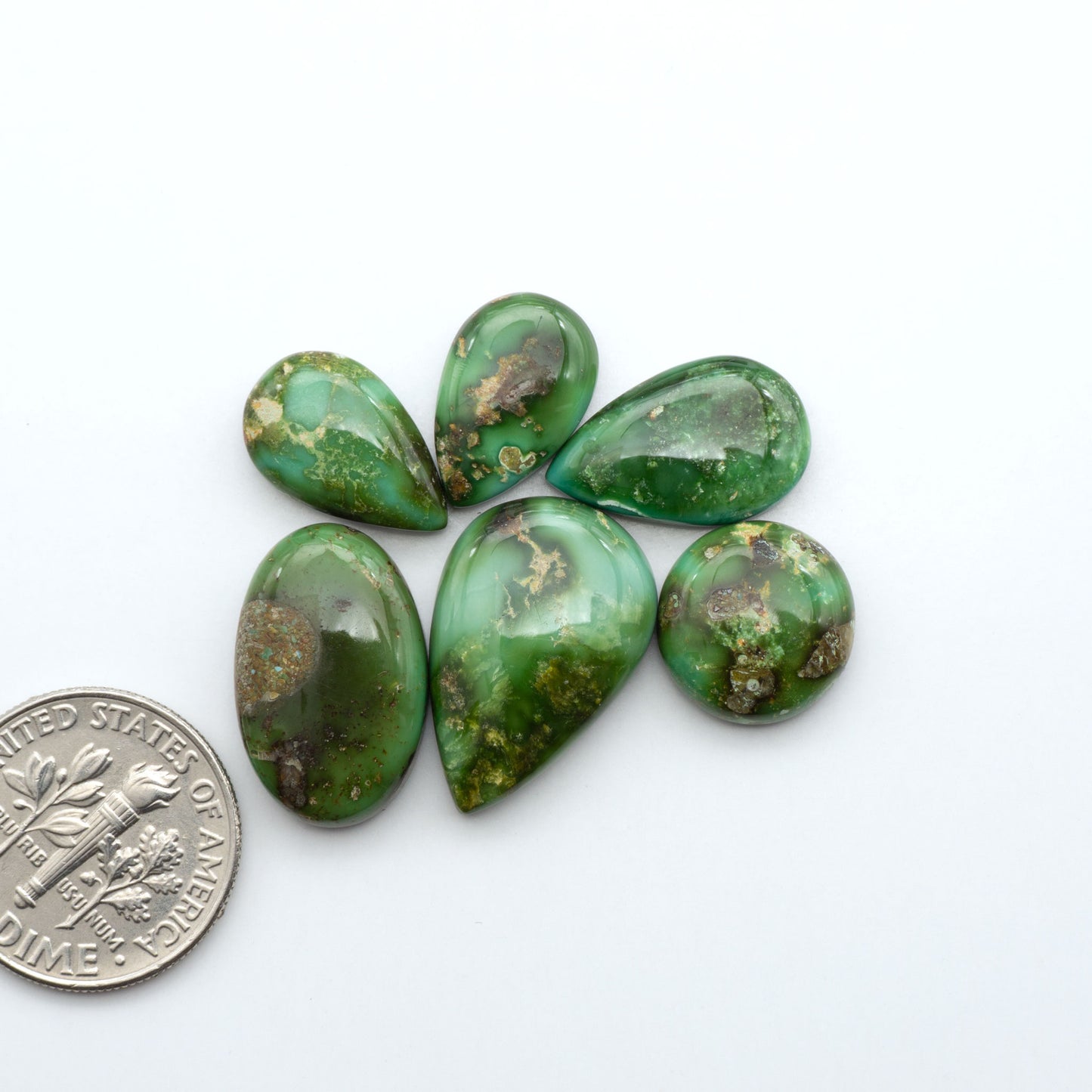 Sonoran Mountain Turquoise cabochons, blue-green color with natural matrix, polished stones on a white background, with a US dime for scale