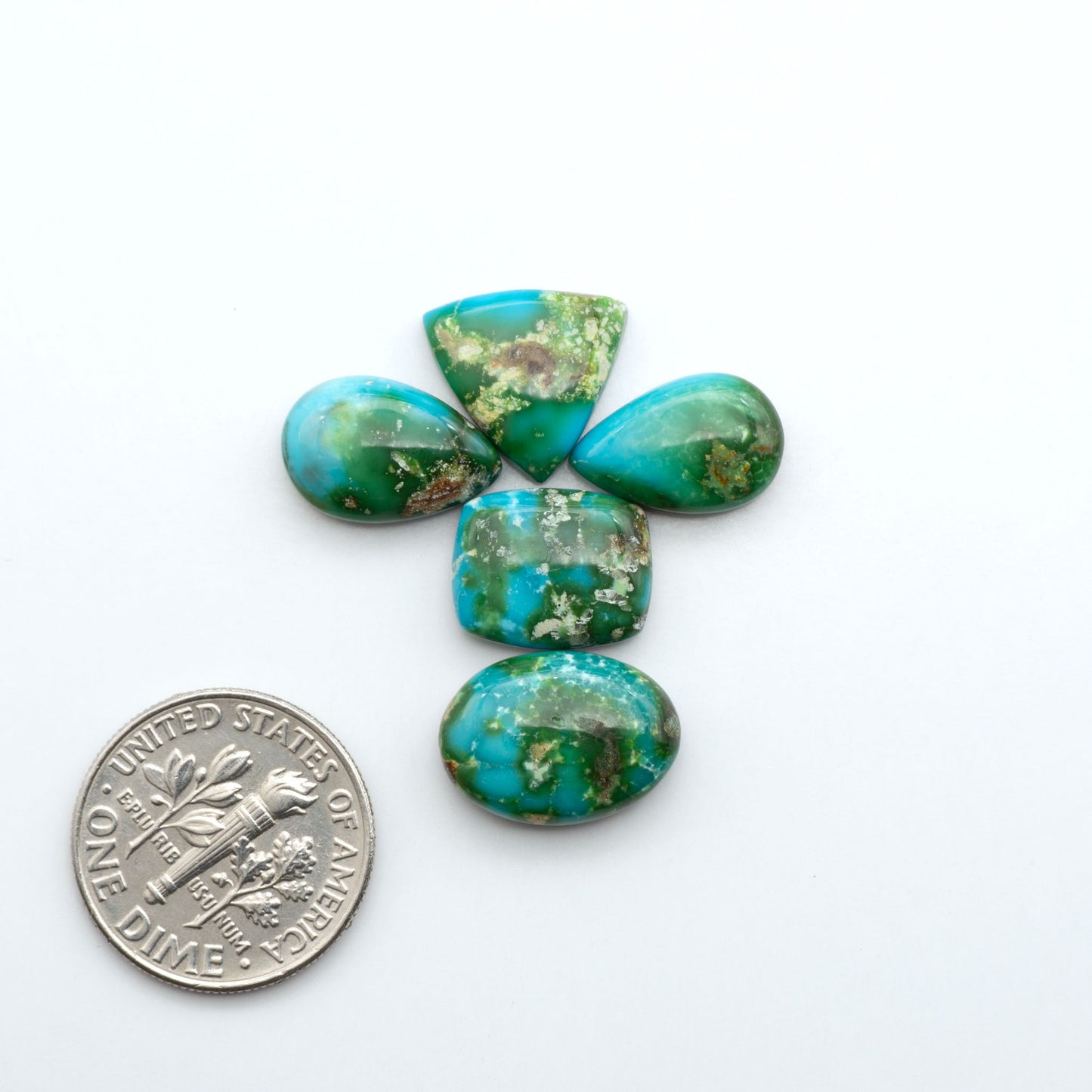 Sonoran Mountain Turquoise cabochons, blue-green color with natural matrix, polished stones on a white background, with a US dime for scale