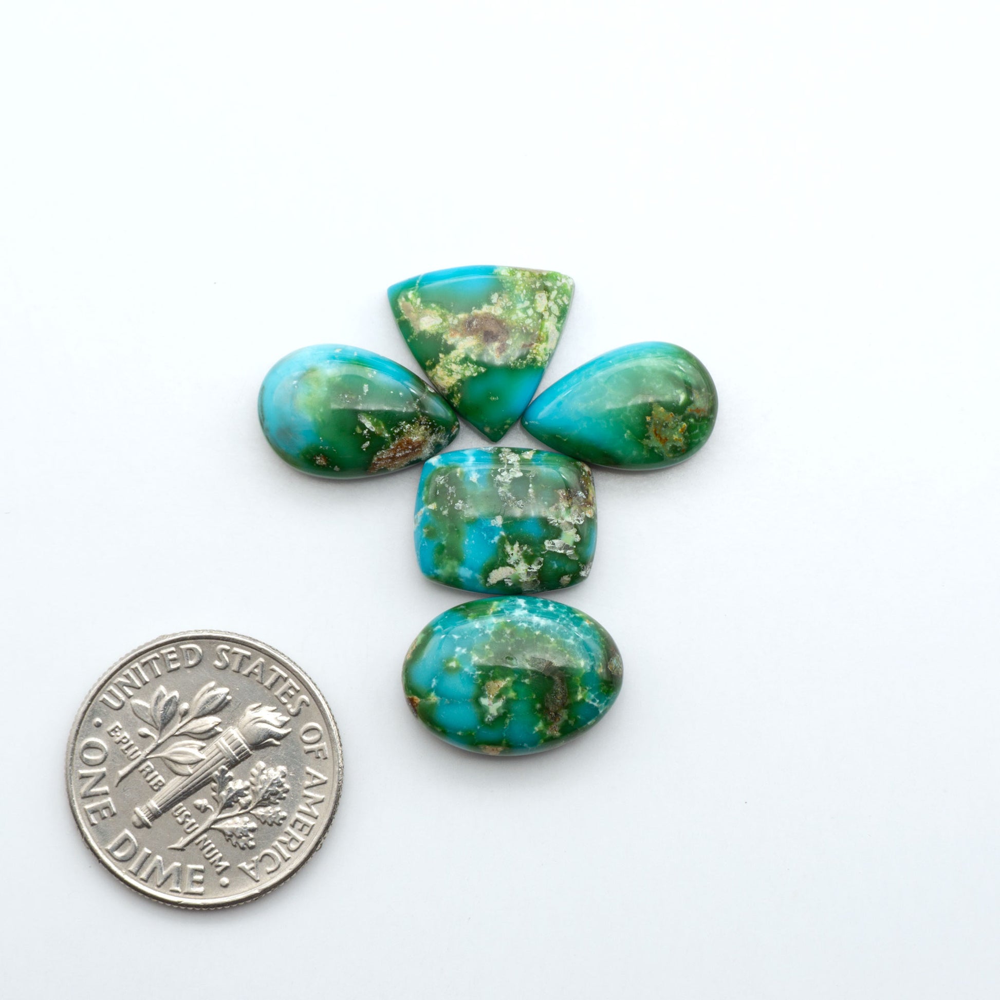 Sonoran Mountain Turquoise cabochons, blue-green color with natural matrix, polished stones on a white background, with a US dime for scale