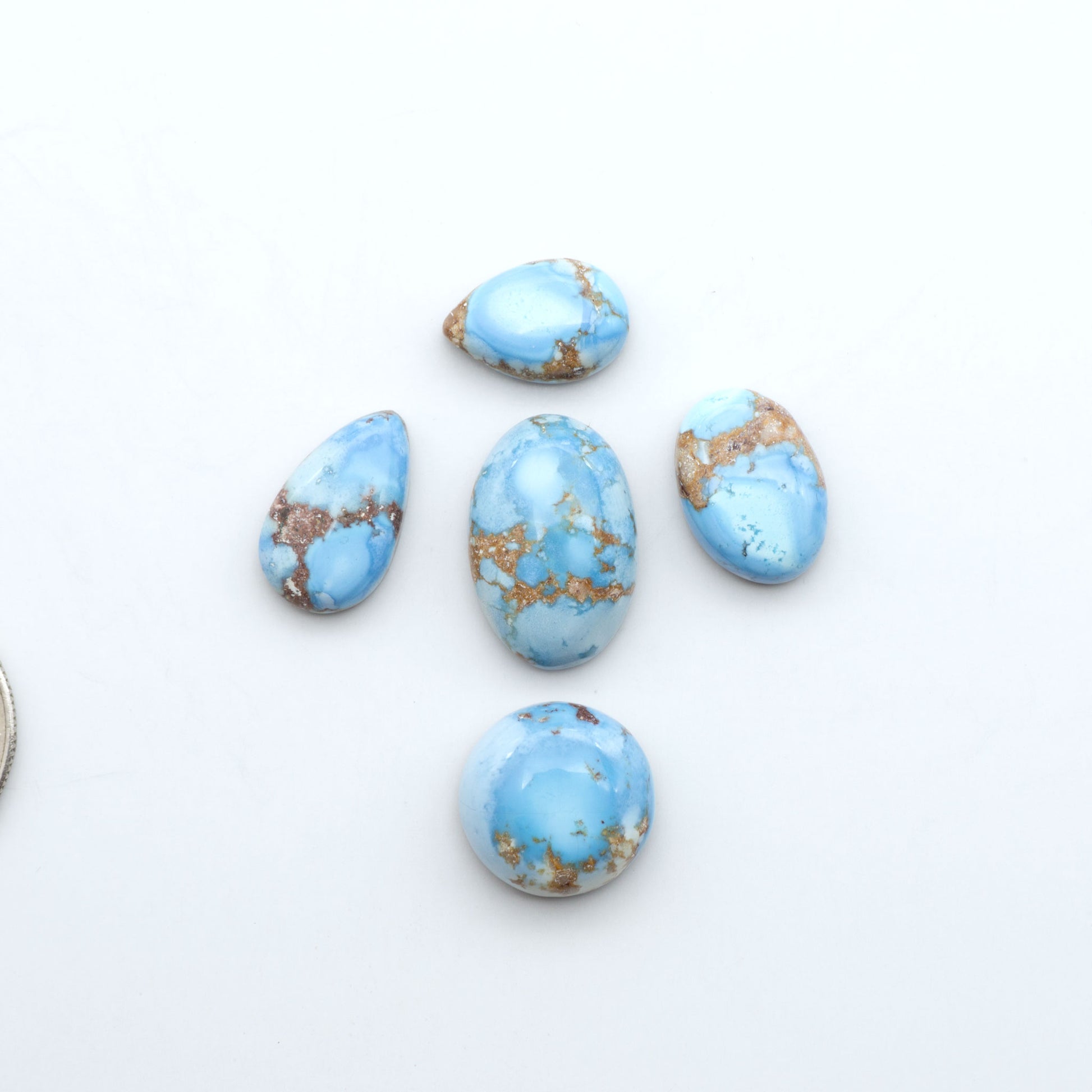 Golden Hills Turquoise cabochons, icy blue to lavender tones with chocolate matrix, polished stones on a white background with a US dime for scale