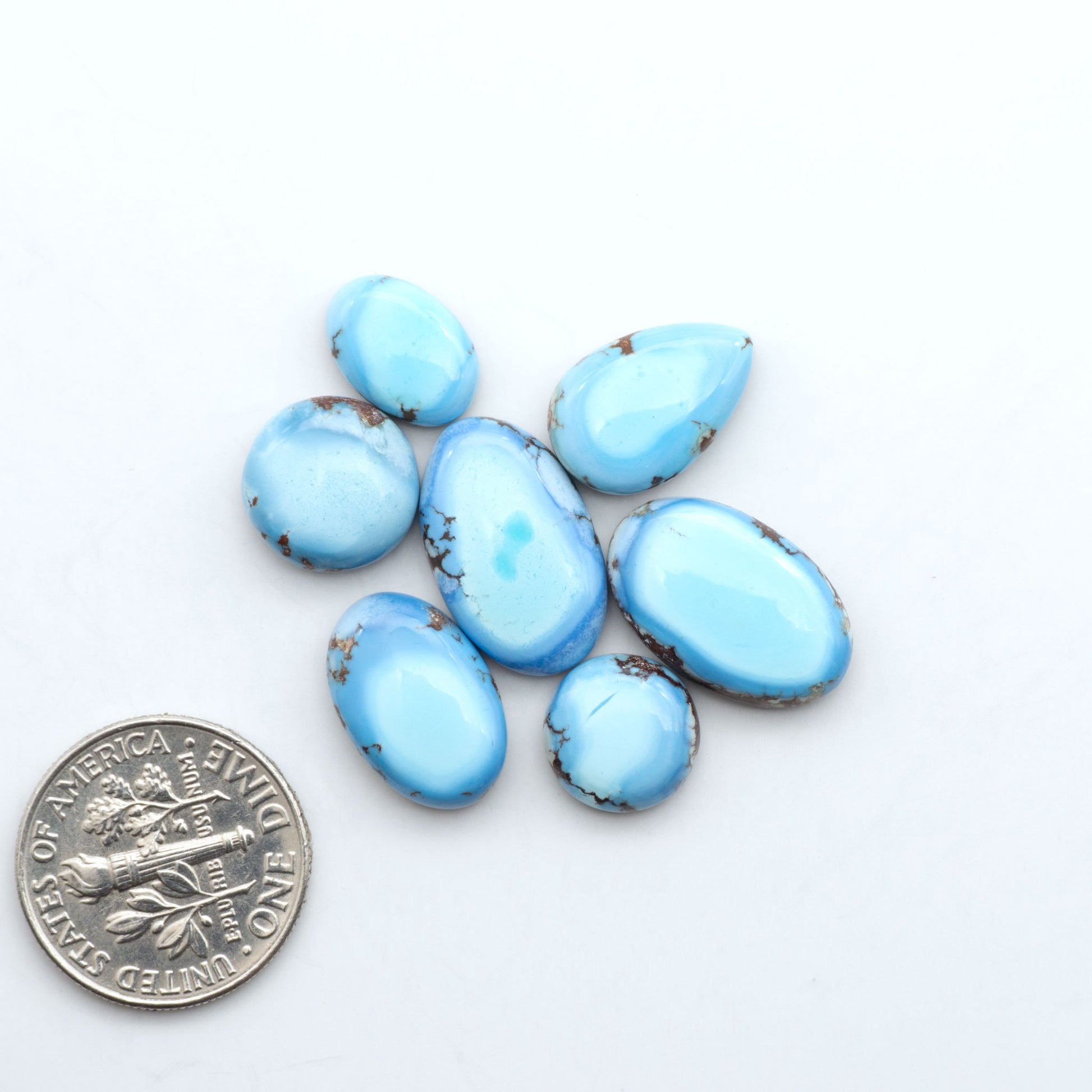 Golden Hills Turquoise cabochons, icy blue to lavender tones with chocolate matrix, polished stones on a white background with a US dime for scale