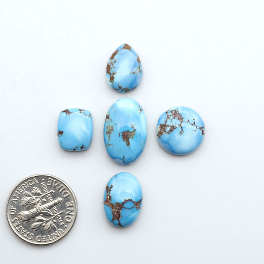 Golden Hills Turquoise cabochons, icy blue to lavender tones with chocolate matrix, polished stones on a white background with a US dime for scale
