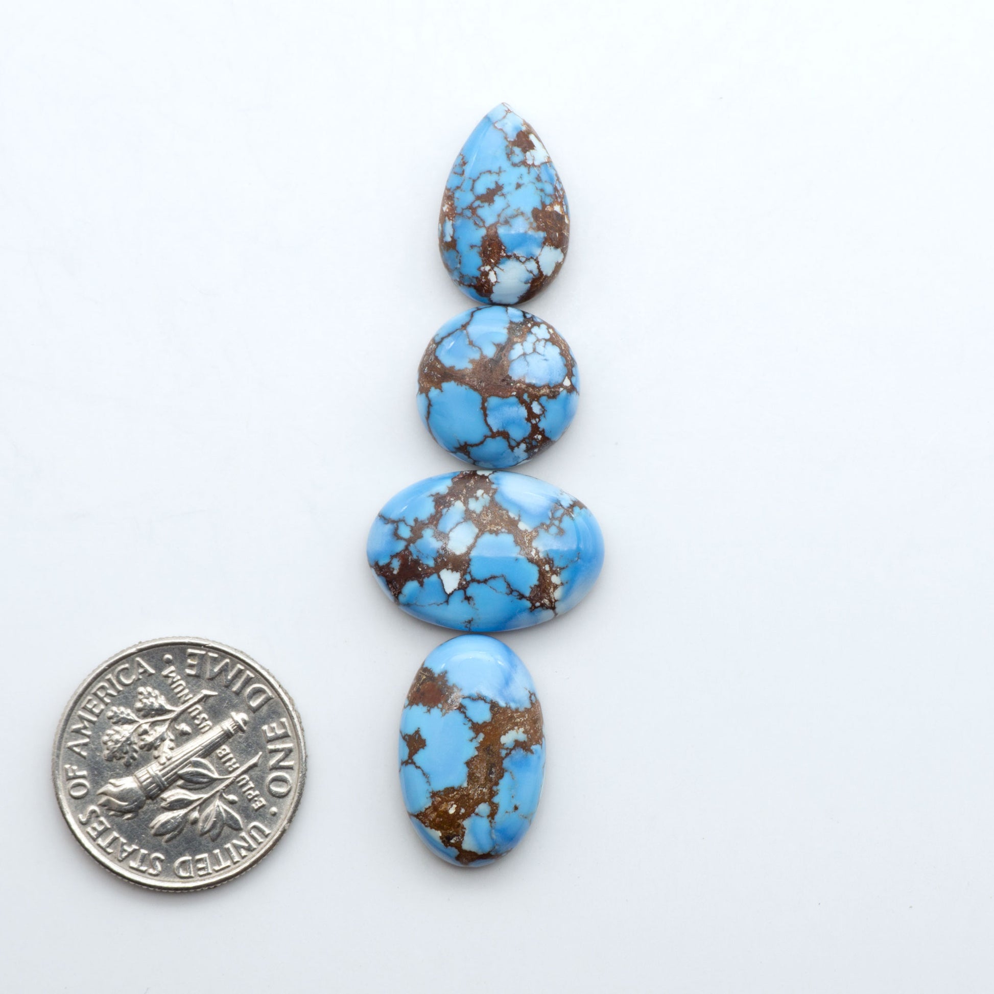 Golden Hills Turquoise cabochons, icy blue to lavender tones with chocolate matrix, polished stones on a white background with a US dime for scale