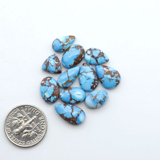 Golden Hills Turquoise cabochons, icy blue to lavender tones with chocolate matrix, polished stones on a white background with a US dime for scale