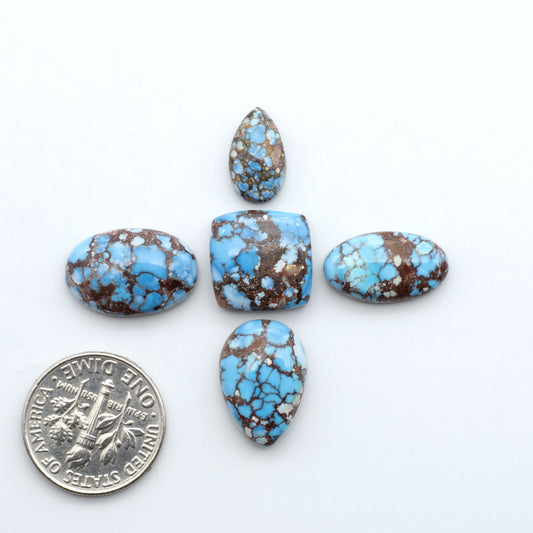 Golden Hills Turquoise cabochons, icy blue to lavender tones with chocolate matrix, polished stones on a white background with a US dime for scale