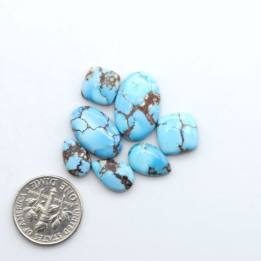 Golden Hills Turquoise cabochons, icy blue to lavender tones with chocolate matrix, polished stones on a white background with a US dime for scale