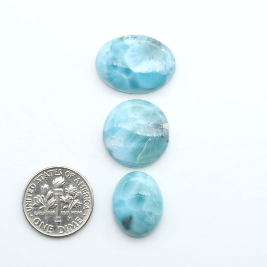 Larimar stone cabochons, cut and polished, blue and white gemstones on a white background, with a US dime for scale