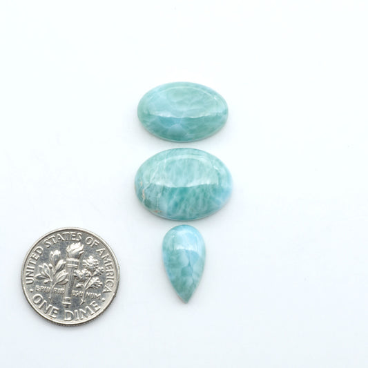 Larimar stone cabochons, cut and polished, blue and white gemstones on a white background, with a US dime for scale