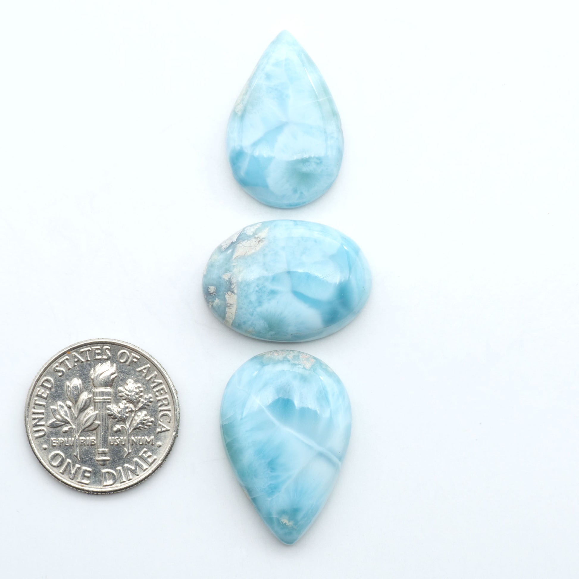 Larimar stone cabochons, cut and polished, blue and white gemstones on a white background, with a US dime for scale