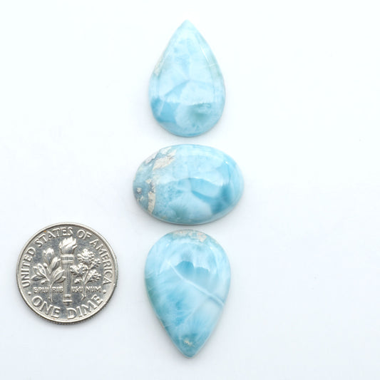 Larimar stone cabochons, cut and polished, blue and white gemstones on a white background, with a US dime for scale