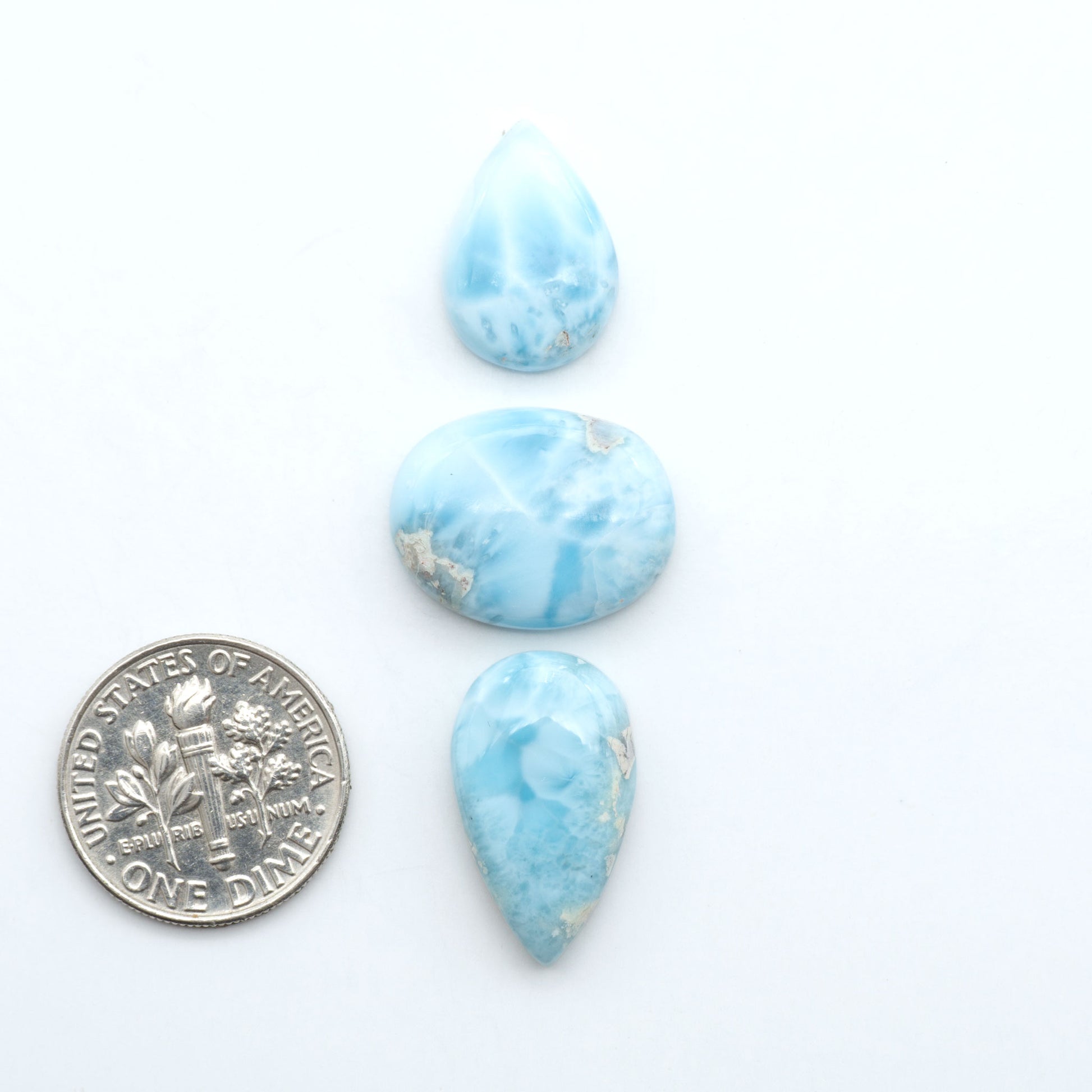 Larimar stone cabochons, cut and polished, blue and white gemstones on a white background, with a US dime for scale