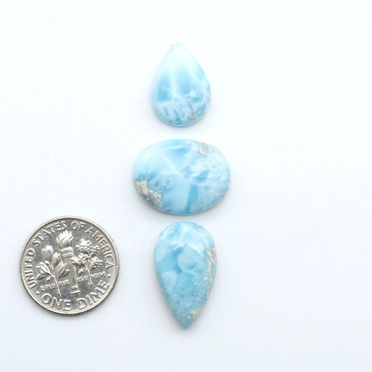 Larimar stone cabochons, cut and polished, blue and white gemstones on a white background, with a US dime for scale