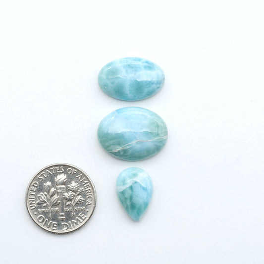 Larimar stone cabochons, cut and polished, blue and white gemstones on a white background, with a US dime for scale