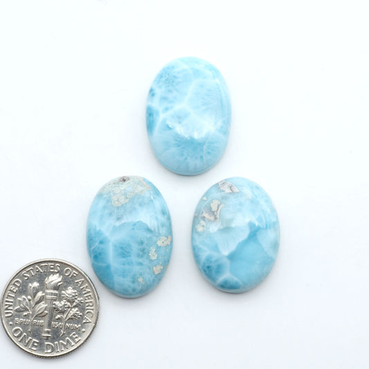 Larimar stone cabochons, cut and polished, blue and white gemstones on a white background, with a US dime for scale