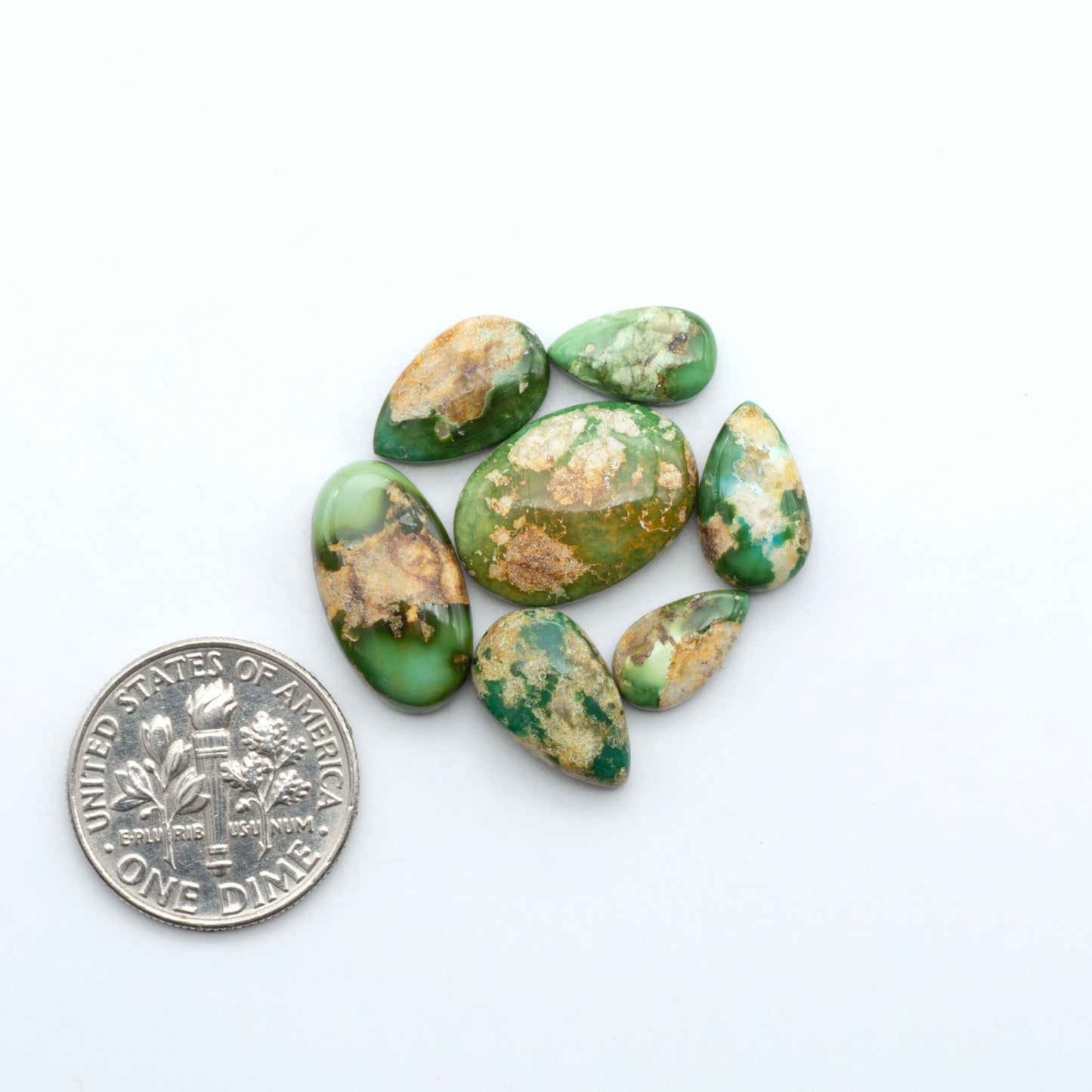 Sonoran Mountain Turquoise cabochons, blue-green color with natural matrix, polished stones on a white background, with a US dime for scale