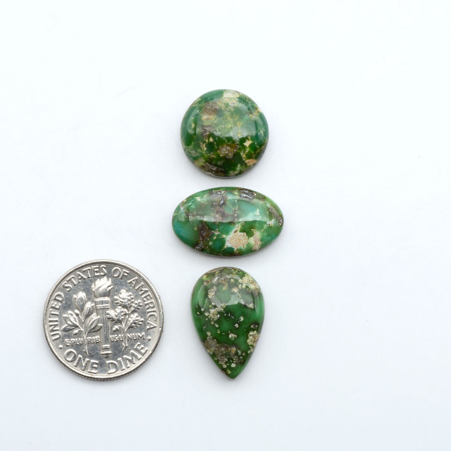 Sonoran Mountain Turquoise cabochons, blue-green color with natural matrix, polished stones on a white background, with a US dime for scale