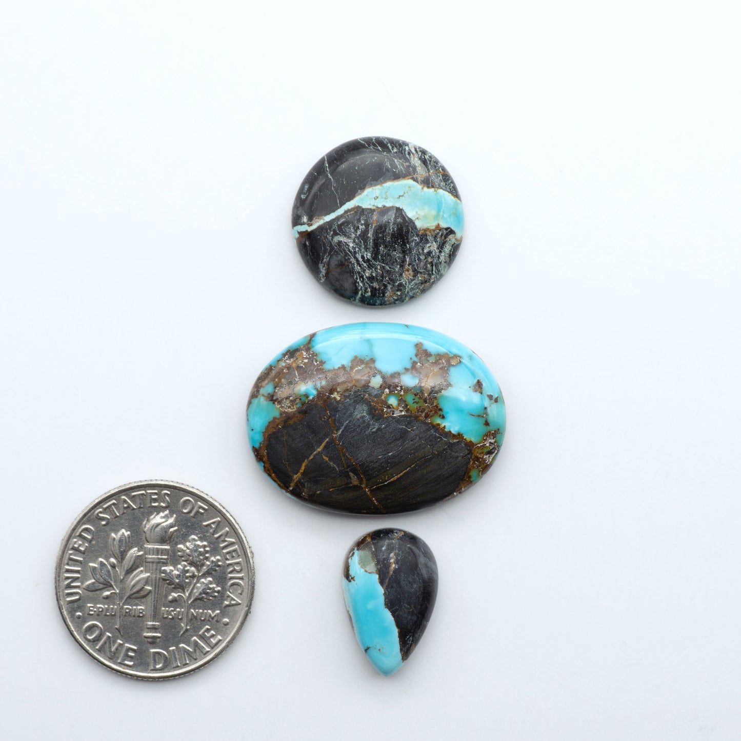 Black Jack turquoise cabochons, blue-green color with black matrix, polished stones on a white background with a US dime for scale