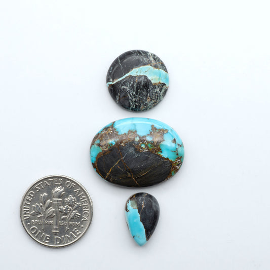 Black Jack turquoise cabochons, blue-green color with black matrix, polished stones on a white background with a US dime for scale