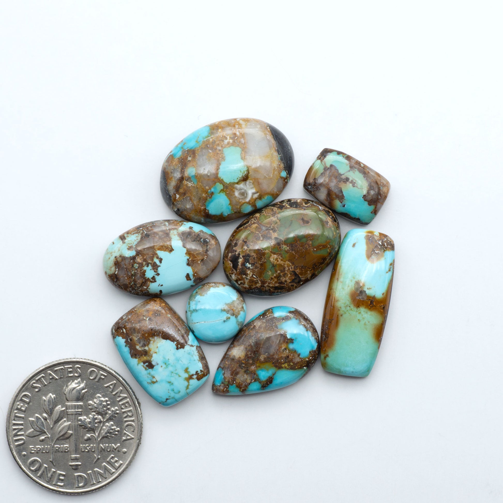 Black Jack turquoise cabochons, blue-green color with black matrix, polished stones on a white background with a US dime for scale