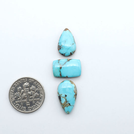 Black Jack turquoise cabochons, blue-green color with black matrix, polished stones on a white background with a US dime for scale