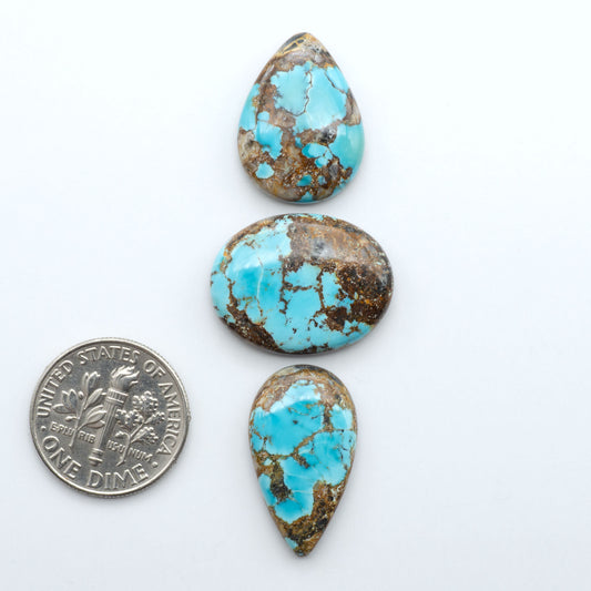 Black Jack turquoise cabochons, blue-green color with black matrix, polished stones on a white background with a US dime for scale
