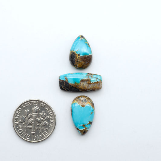 Black Jack turquoise cabochons, blue-green color with black matrix, polished stones on a white background with a US dime for scale