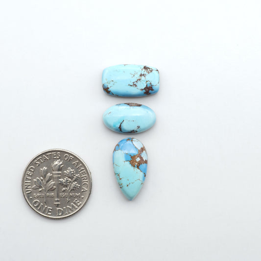 Golden Hills Turquoise cabochons, icy blue to lavender tones with chocolate matrix, polished stones on a white background with a US dime for scale