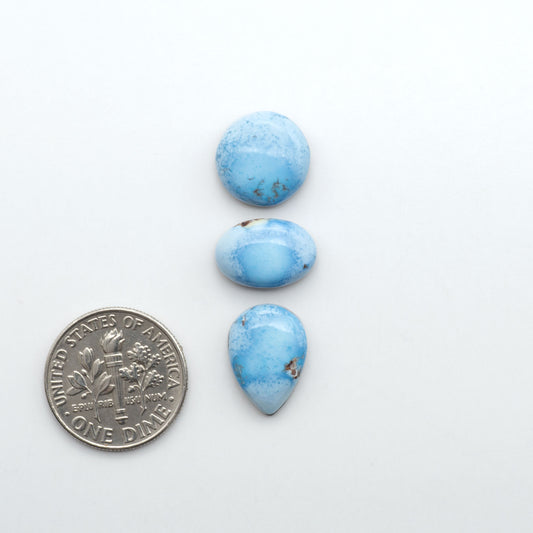 Golden Hills Turquoise cabochons, icy blue to lavender tones with chocolate matrix, polished stones on a white background with a US dime for scale