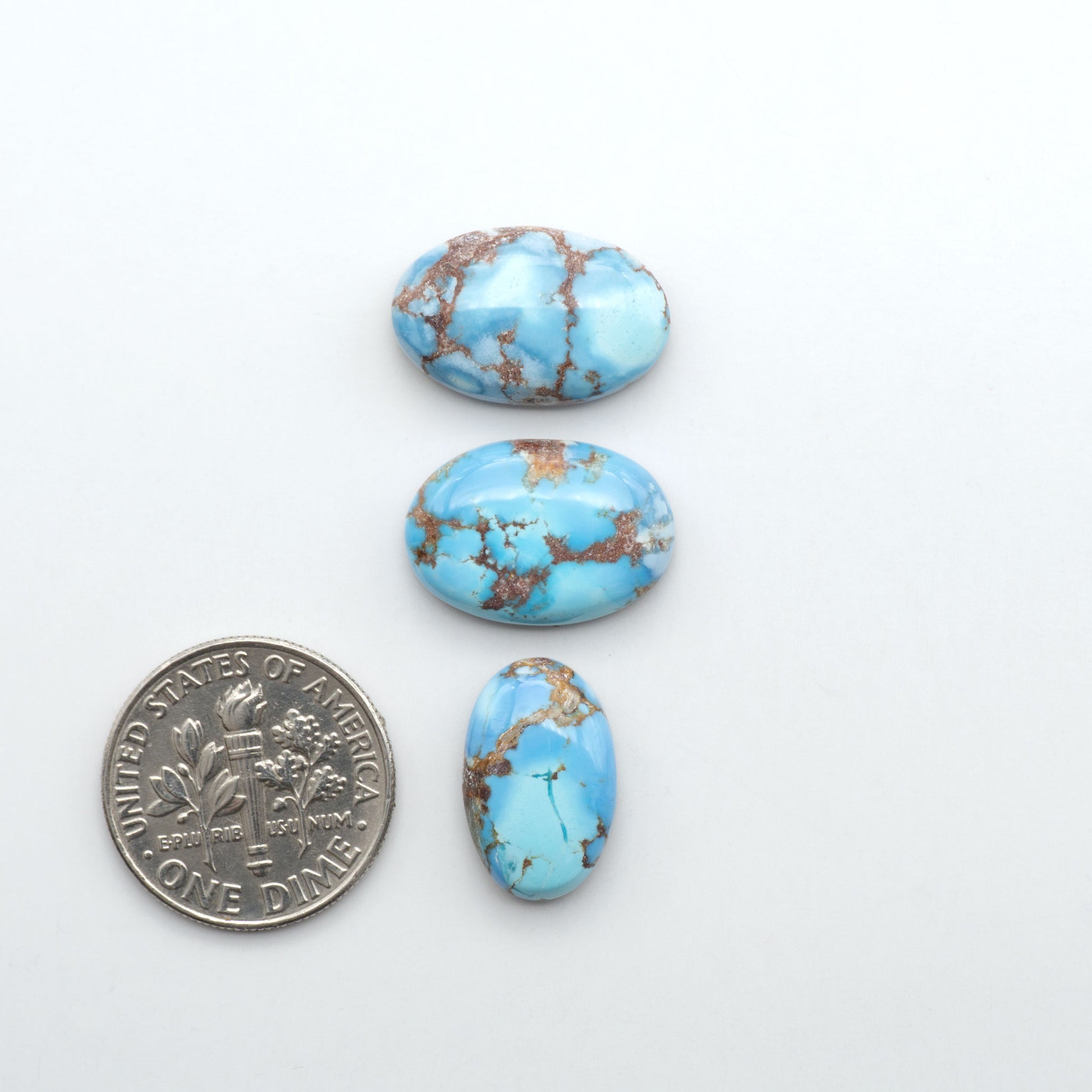 Golden Hills Turquoise cabochons, icy blue to lavender tones with chocolate matrix, polished stones on a white background with a US dime for scale